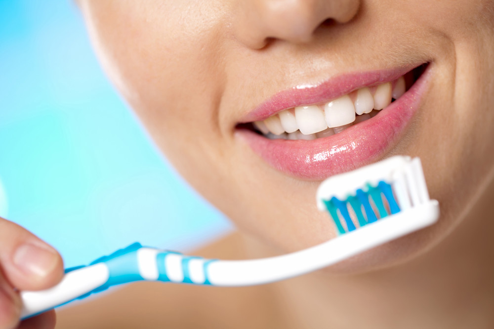 Close-up of a smiling adult holding a toothbrush with toothpaste.